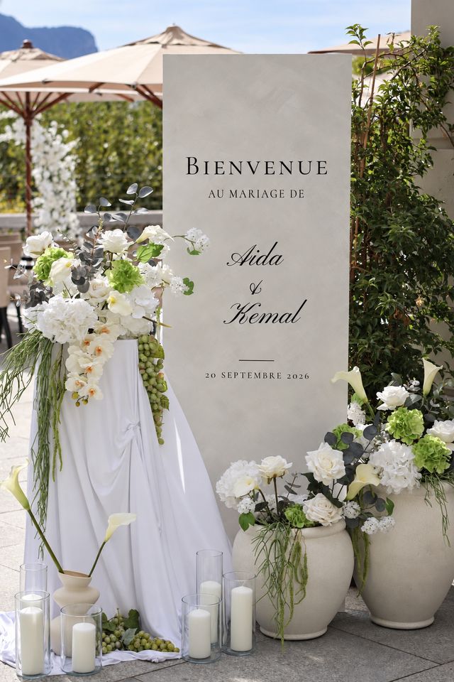 Panneau d'accueil de mariage entouré de compositions florales blanches et vertes et de bougies