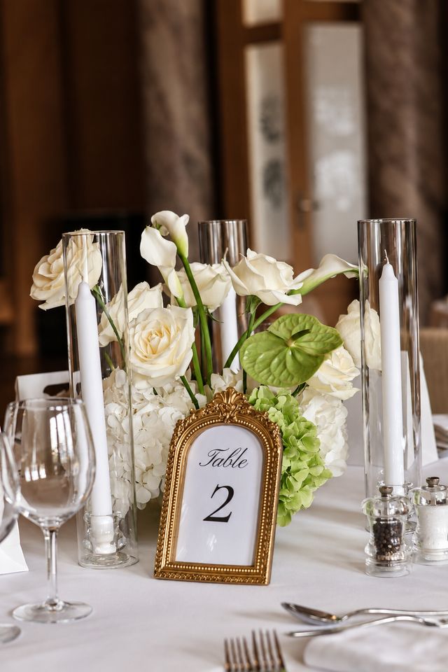 Centre de table de mariage avec roses blanches, arums, anthurium vert et numéro de table dans un cadre doré
